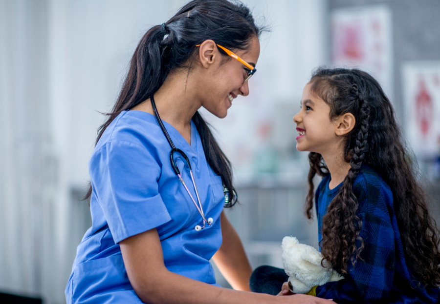 HCP and young girl sat on a hospital bed smiling at eachother